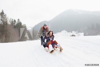 Happy young couple sledding in snowy field