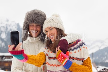 Happy young couple taking selfie with smart phone in snow