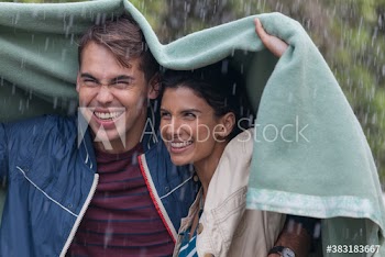 Happy young couple under blanket in rain