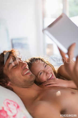 Happy young couple using digital tablet on bed