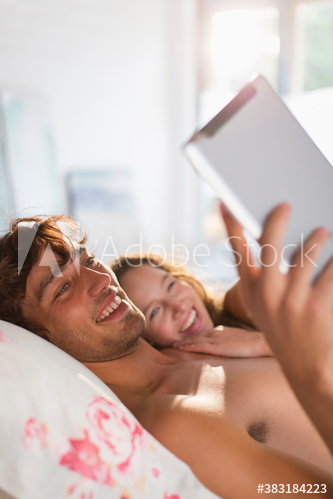 Happy young couple using digital tablet on bed