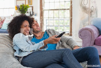 Happy young couple with remote control watching TV on beanbag chair