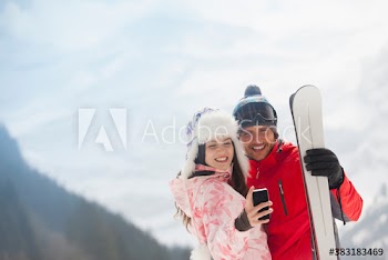 Happy young couple with skis taking selfie in snow