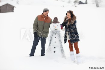 Happy young couple with snowman in snowy field