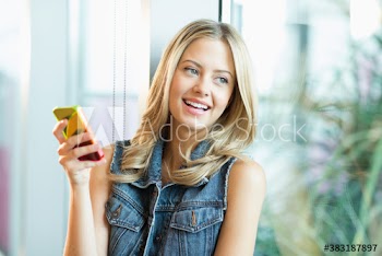 Happy young female college student using smart phone in window