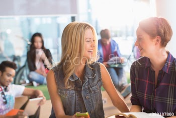 Happy young female college students talking in student lounge