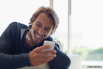 Happy young man laughing and using smart phone