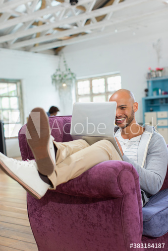Happy young man using laptop in armchair