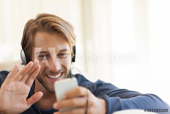 Happy young man video chatting with smart phone and headphones