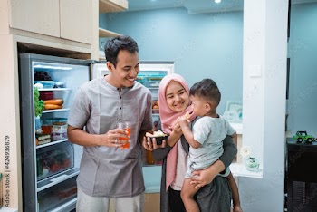 happy young muslim family having iftar breaking the fast while standing in the kitchen eating dates fruit