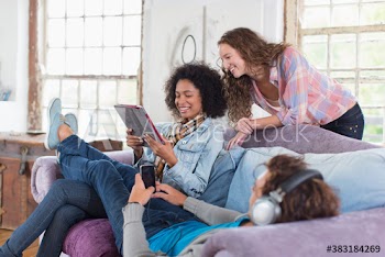 Happy young roommates using digital tablet and listening to music on sofa