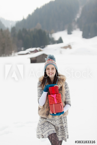 Happy young woman carrying Christmas gifts in snowy field
