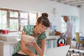Happy young woman eating cereal at laptop in kitchen