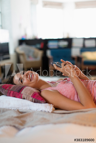 Happy young woman listening to music on bed