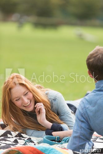 Happy young woman on blanket with boyfriend in park
