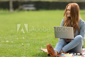 Happy young woman using laptop on blanket in grass at park