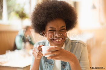 Happy young woman with afro drinking coffee in cafe
