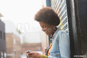 Happy young woman with afro using smart phone on city street