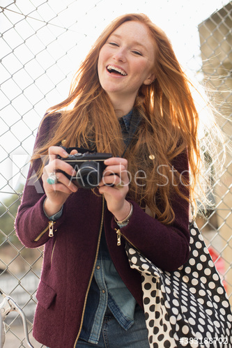 Happy young woman with camera at chainlink fence