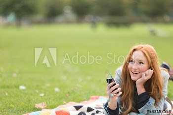 Happy young woman with mp3 player on blanket in park