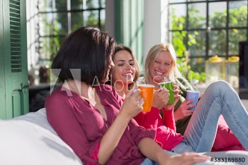 Happy young women friends drinking tea on sofa
