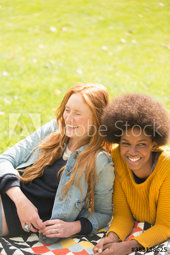 Happy young women friends laughing on blanket in sunny grass