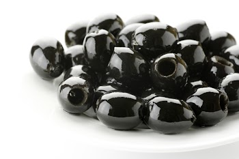 Heap of black olives in white plate on white background.