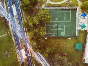 high angle photo of green lawn tennis court near trees, road, and railway