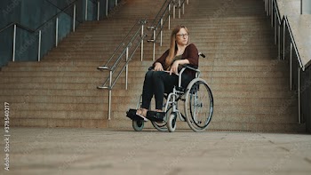 Hopeless young woman in the wheelchair in front of the inaccessible stairs. High quality photo