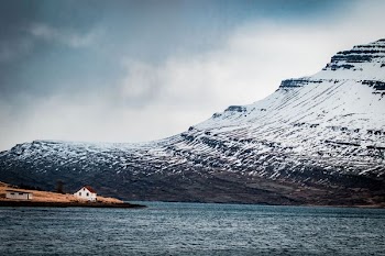 house on island near snow covered mountain at daytime