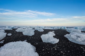 ice on black rocks under white clouds and blue sky