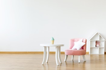 Kid's table and chair with a star pillow in a white, empty room interior with a dollhouse in the background. Place for your product