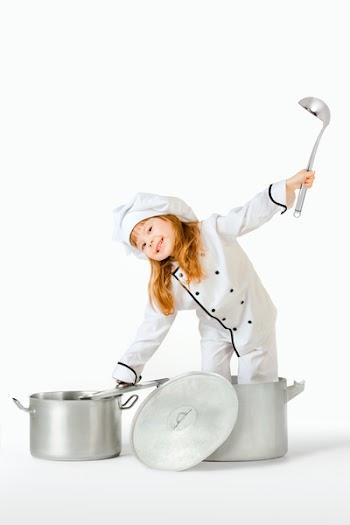 Kitchen hand. A little pretty girl dressed as a kitchen hand in a cooking pot holding a top and a ladle.