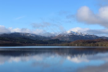 Lake Near Green Trees With Overlooking Mountain Peaks