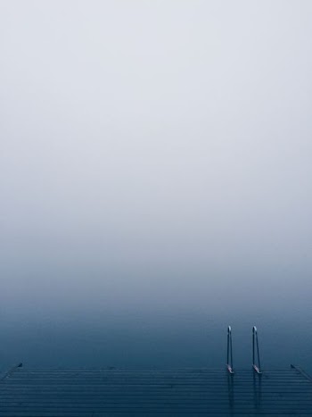 Lake pier with a ladder on serene waters on a foggy day