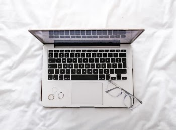 Laptop and Glasses on White Bed