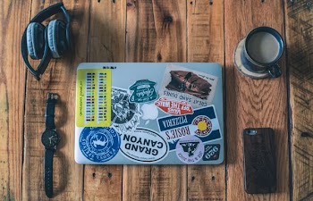 laptop near watch, headphones, phone and cup of coffee on brown wooden table