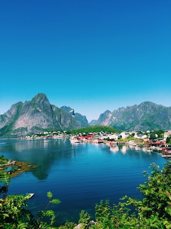 Large Body of Water Across Village and Mountains Under Blue Skies