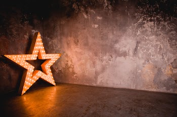 Large wooden star with a large number of lights are lit. Beautiful decor, design. Loft style Studio. Dark concrete background. Christmas, holiday, honorary star. Five stars 5 stars