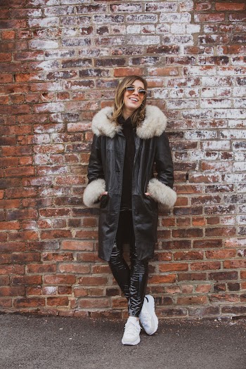 Laughing Woman Wearing Black Coat And Sunglasses Standing Against The Wall