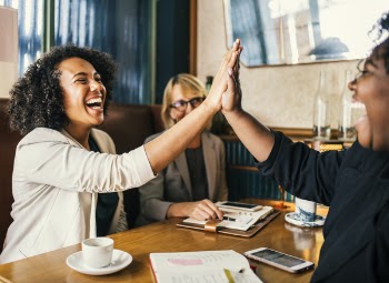 Laughing Women Sitting in Front of Table Doing High Five Clap