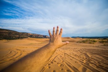 left human hand about to reach sand and sky