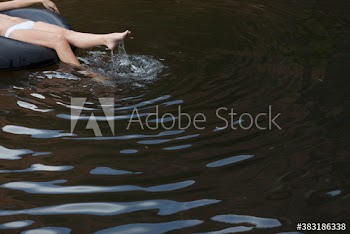 Leg of young woman on inner tube splashing in lake water