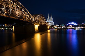Lighted City Skyline Across River With Metal Bridge