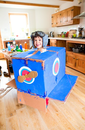 Little boy dressed as a pilot plays in his homemade cardboard box...