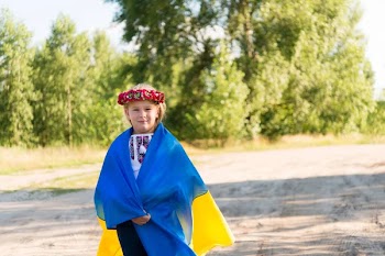 Little girl in national Ukrainian clothes - vyshyvanka. Ukraine, field. In the hands of the flag of Ukraine.