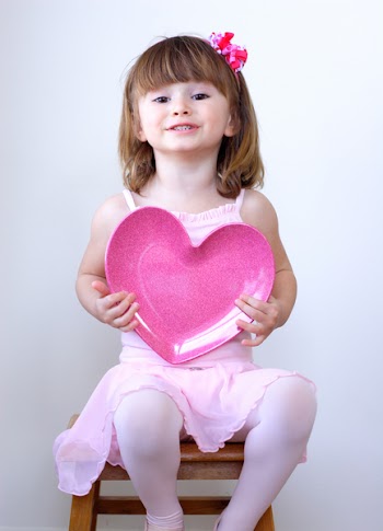 Little girl in pink holding a heart over the light background