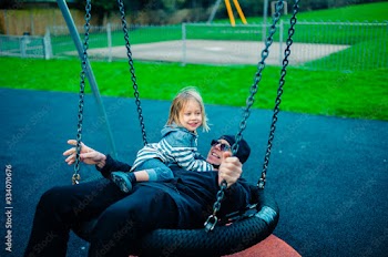 Little preschooler playing with his grandfather on spider swing in park