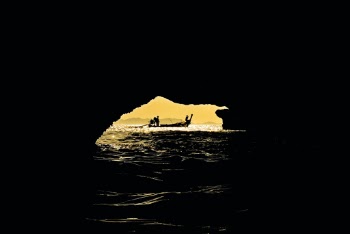 Long tail boat riding on the sea, visible through cave