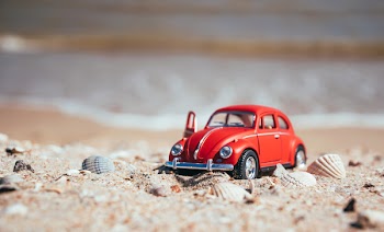 Los Angeles, California / USA - August 11 2018: A 1:18 scale model of a beautiful red  Volkswagen Beetle made by Auto Art on the background of a sandy sunny beach in Los Angeles, California, USA